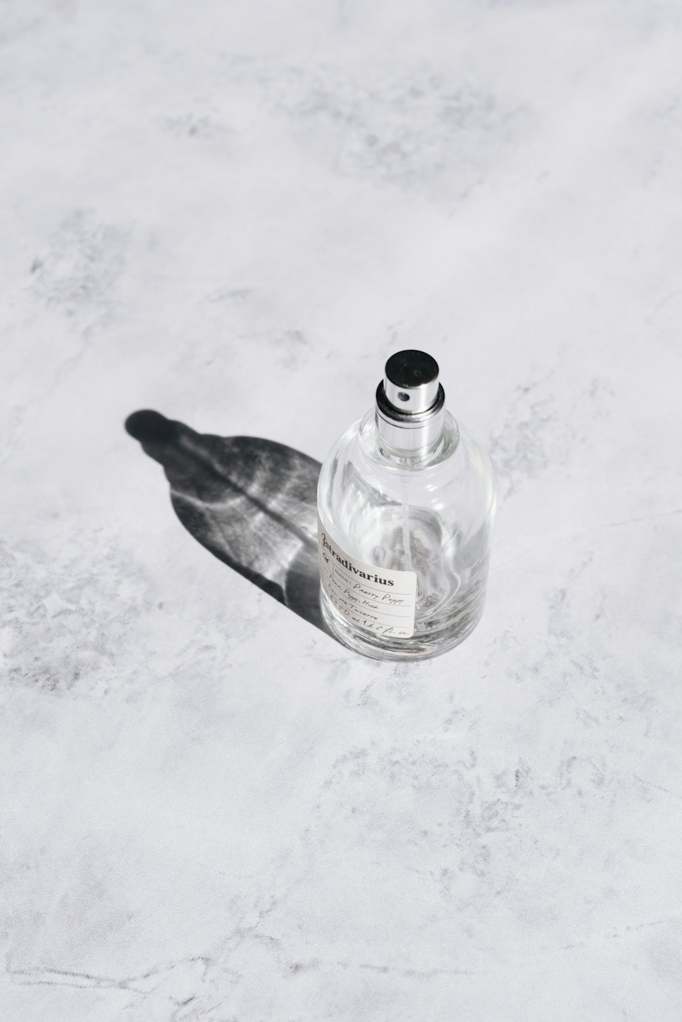 Una boccetta di profumo con tappo argento e nero su marmo.